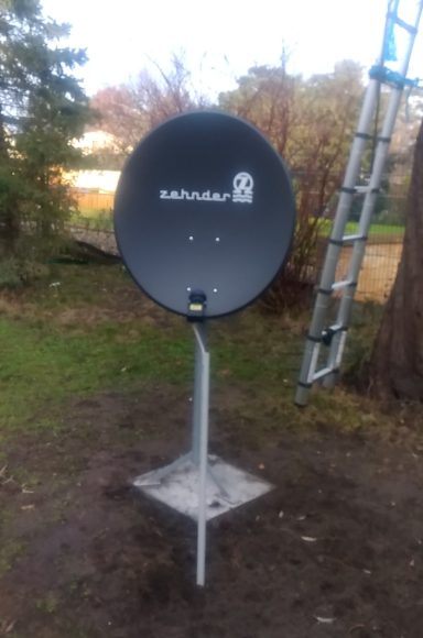 Schwarze Satellitenschüssel auf einem Standfuß in einem Garten.